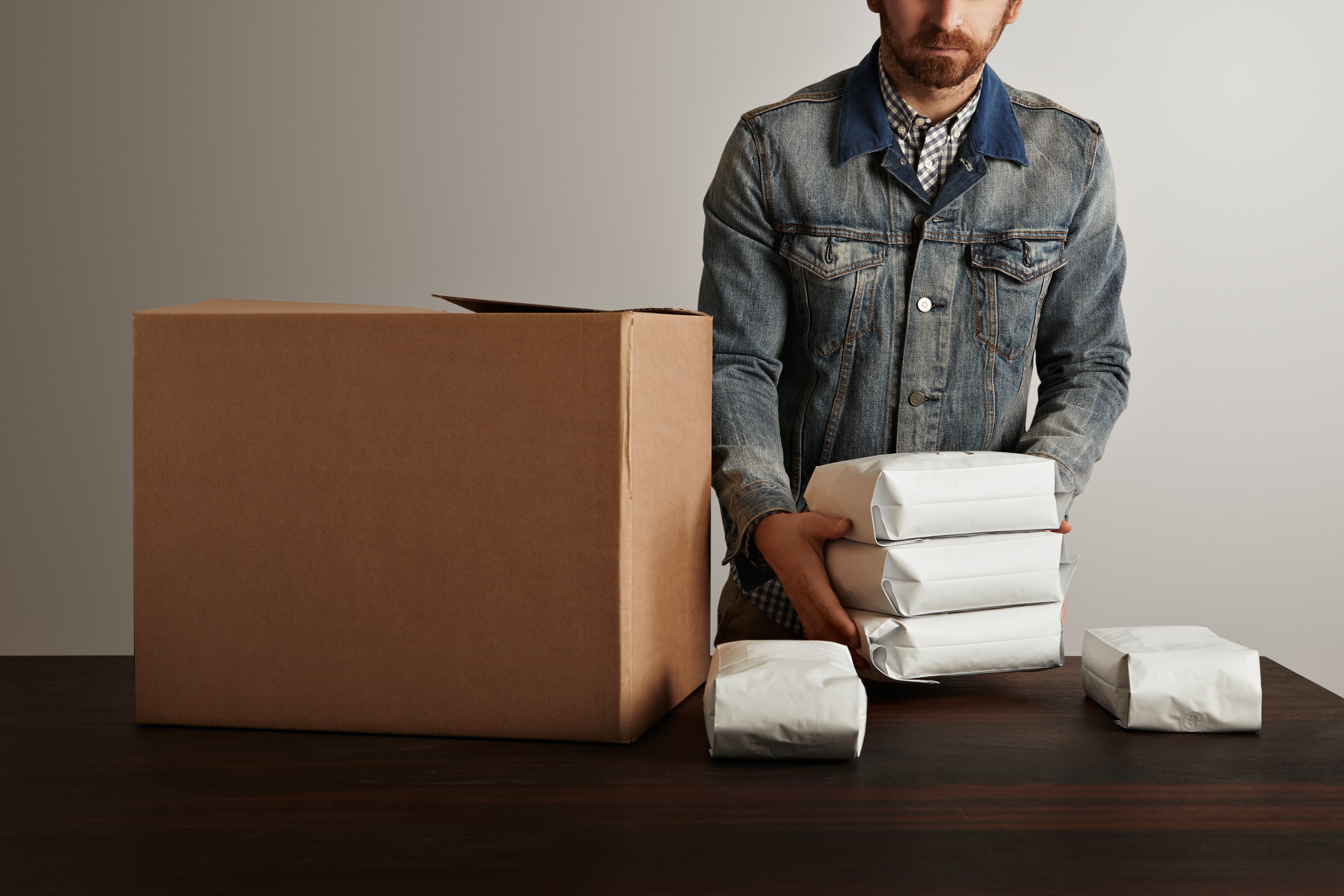 bearded-brutal-man-jeans-work-jacket-puts-blank-sealed-hermetic-packages-inside-big-carton-paper-box-wooden-table-special-delivery.jpg